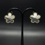 Close-up of flower-shaped stud earrings with half white and half grey shell inlay in gold setting studs.
